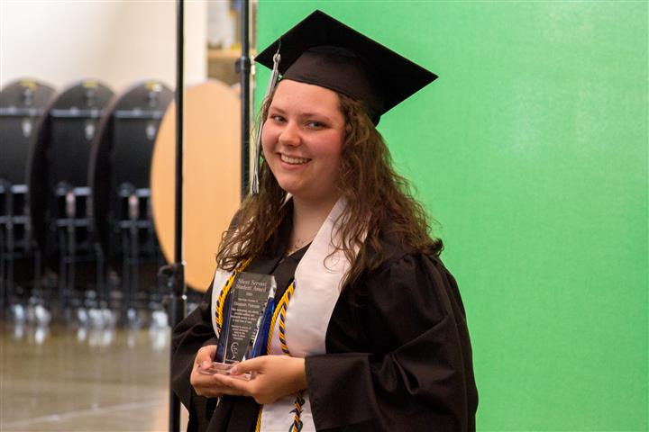 Elizabeth holds up her award smiling. 